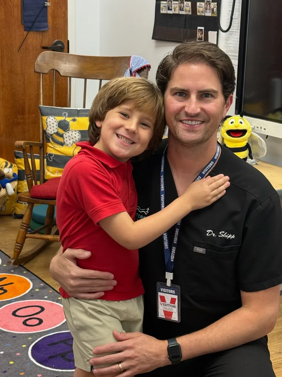 Dr. Patrick Shipp in Rabbit Creek Dental scrubs holding his son during career day at his son's school